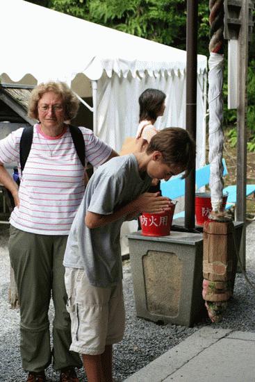 Peter bows respectfully in front of a Buddist temple, while his grandmother looks on.